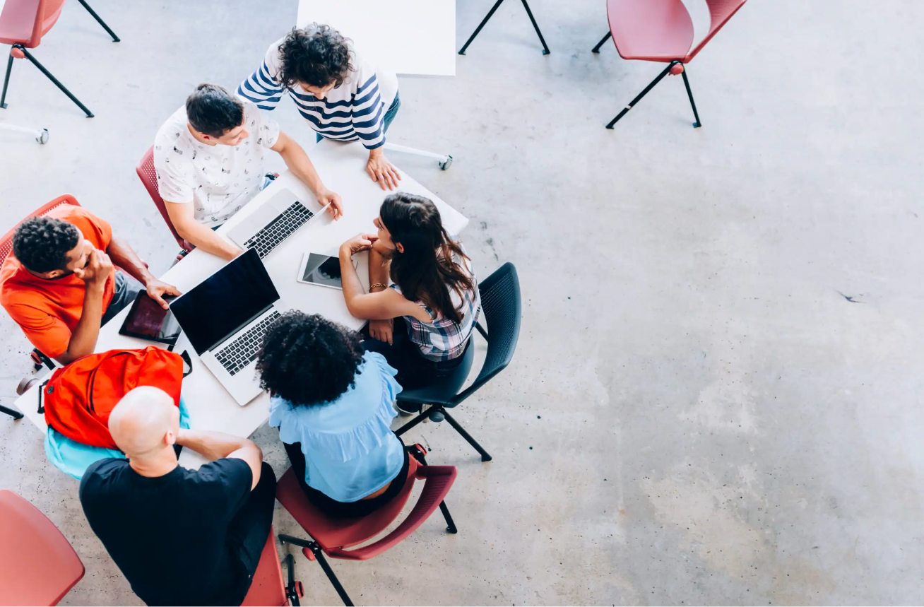 An aerial photo of a small group of 6 students collaborating on a project with their digital devices.